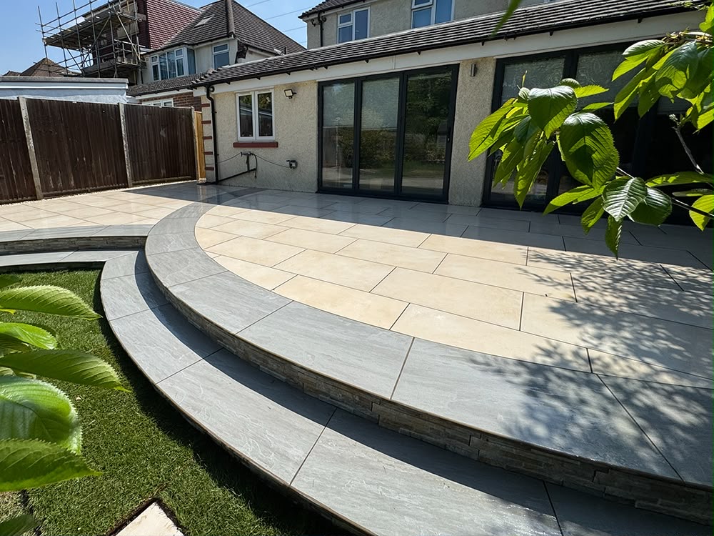 Curved two-level porcelain patio with steps leading down to a new lawn