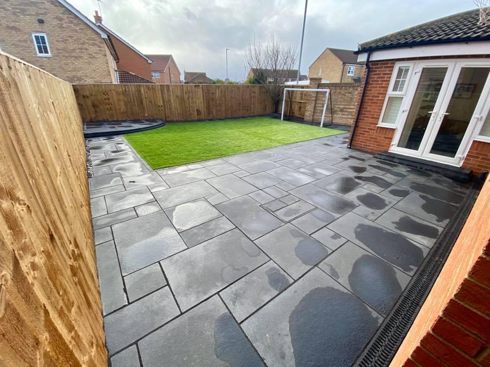 Charcoal slab patio with new lawn and fencing behind a brick house