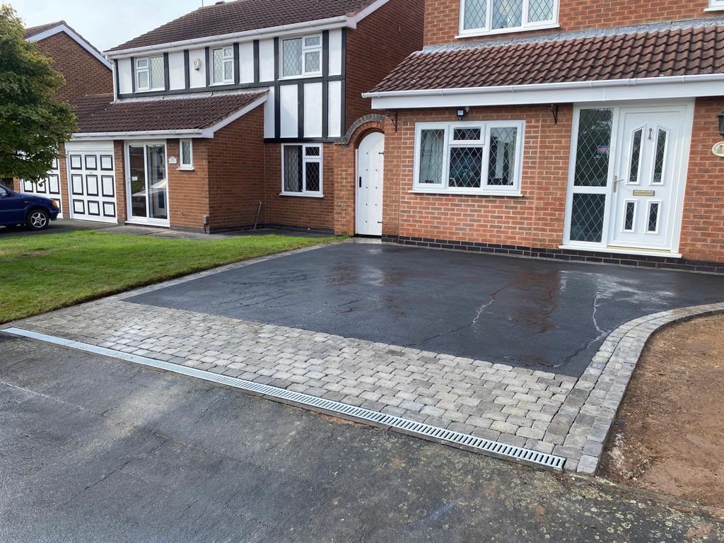 New tarmac driveway with a block paved border and drainage channel in front of a brick house