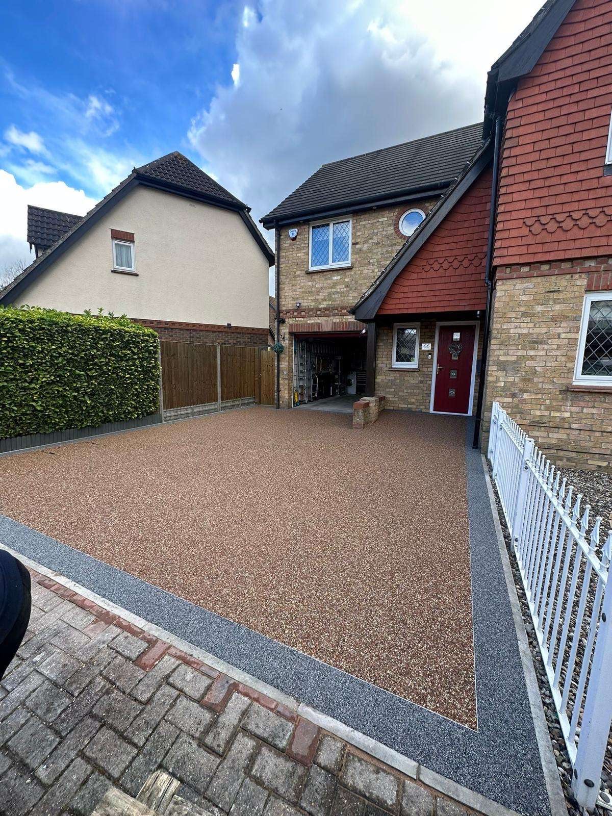 Resin driveway with charcoal edging beside a white fence and a brick and tile house