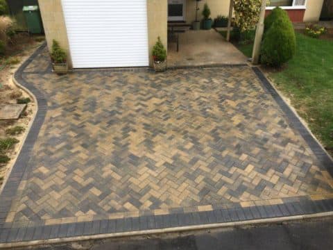 Buff herringbone block paved driveway with a charcoal border up to a garage