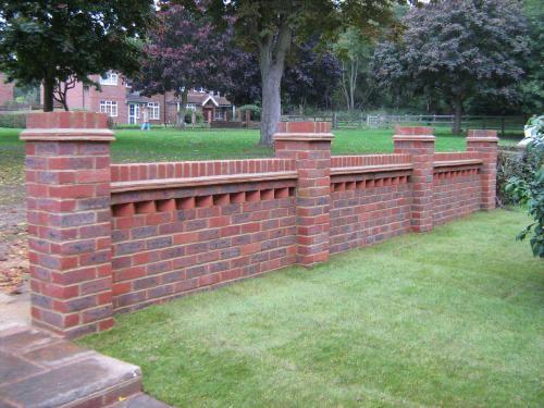 Red brick front wall with piers and decorative coping beside a lawn