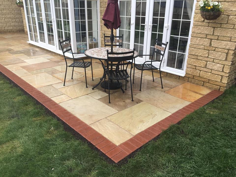 Sandstone patio with red brick edging and garden furniture outside French doors